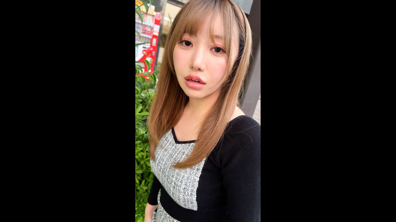 街角の植え込みの前で、黒とグレーの服を着た女性を正面から捉えた近距離のカット。
