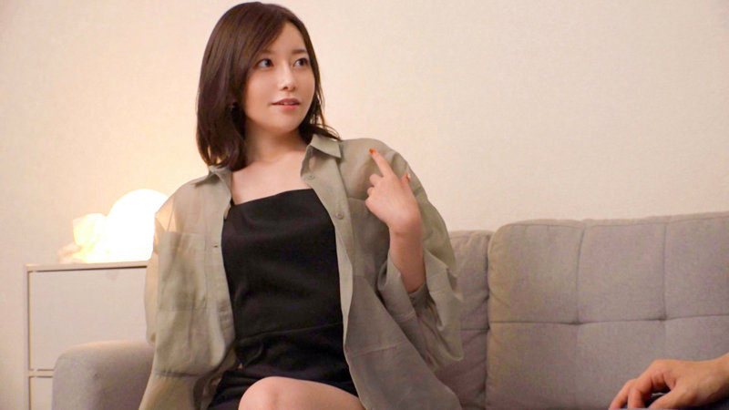 さちかがグレーシャツ+黒ミニワンピース姿でソファに腰掛け、リラックスした表情を見せる素人感のある室内シーン